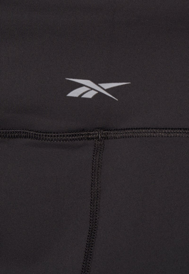 Czarne legginsy sportowe o gładkiej fakturze, z logo Reebok w kolorze srebrnym i widocznym szwem wzdłuż szwów.