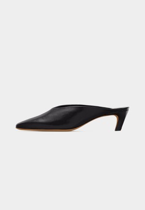 Μαύρο δερμάτινο mule με μυτερή μύτη, στυλ slip-on και χαμηλό κυρτό τακούνι σε λευκό φόντο.