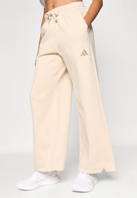 Bézs színű, széles szárú melegítőnadrág gumis derékrésszel és oldalzsebekkel. Bal oldalon tónusos hímzett logóval.