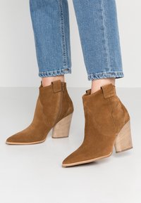 Bottines en cuir suédé marron avec des pointes effilées, des fermetures éclair latérales et des talons empilés. Caractéristiques de points de couture décoratifs et d'un talon texturé.