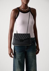 Borsa a tracolla in pelle nera trapuntata con catena e chiusura a pattina, caratterizzata da una forma rettangolare e una superficie liscia.