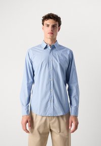 Camisa de manga longa azul clara com colarinho abotoado, apresentando um logótipo subtil no peito e botões brancos, feita de um tecido suave.