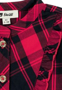 Camicia a quadri rossa e nera con dettagli arricciati, chiusura con bottoni e etichetta "Steiff". Realizzata in tessuto morbido con una texture liscia.