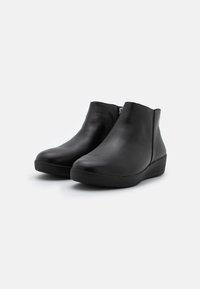 Botas de tobillo de cuero negro con punta redonda y un tacón bajo en cuña. Presentan una cremallera lateral y una textura suave en toda su superficie.