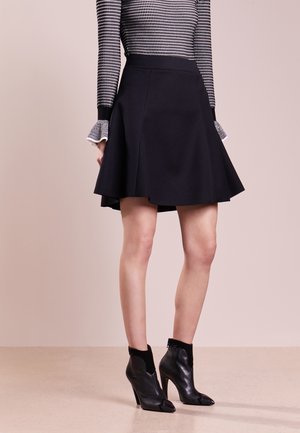 Musta liehuva hame sileällä tekstuurilla, yhdistetty mustiin nilkkakorkokenkiin, joissa on terävät varvassuut ja korot, sekä pitkähihainen kuvioitu paita.