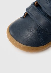 Ναυτικό μπλε δερμάτινο παπούτσι με λεία υφή και λαστιχένια σόλα. Διαθέτει δύο λουράκια με βέλκρο, στρογγυλερή μύτη και διακριτικές ραφές.