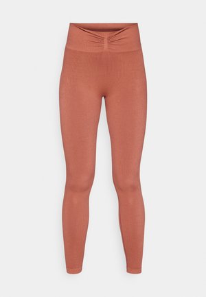 Rust-colored leggings with a fitted design, high waistband, and a gathered detail at the center front. Made of stretchy fabric.