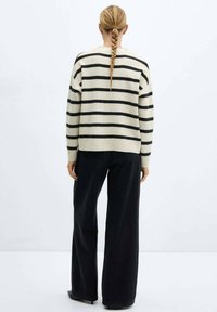 Sweter w paski w kolorze kremowym i czarnym, o luźnym kroju i ściągaczach. Połączony z czarnymi, szerokimi spodniami z wysokim stanem.