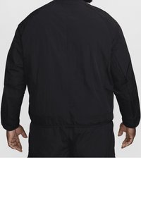 Svart nylonjacka med rundad halsringning, elastiska ärmslut och en slät yta. Har en avslappnad passform och minimalistik design.