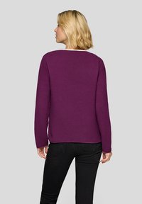 Lila strukturiertes Sweatshirt mit rundem Ausschnitt und langen Ärmeln, kombiniert mit schwarzen Jeans, von hinten gegen einen grauen Hintergrund gezeigt.