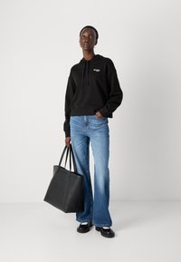 Hoodie noir court avec un logo à l'avant, associé à un jean évasé bleu clair. Un sac fourre-tout en cuir noir et des chaussures noires chunky complètent le look.