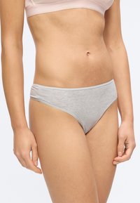 Γυναίκα που φορά ανοιχτό γκρι βαμβακερό εσώρουχο στυλ μπικίνι και απαλό ροζ σουτιέν, εμφανίζεται από τη μέση έως το πάνω μέρος των μηρών, με φόντο ένα μονόχρωμο υπόβαθρο.