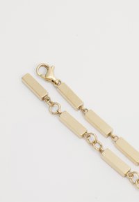 Gold-colored chain bracelet featuring rectangular links and a clasp. The surface is smooth with a matte finish and minimal detailing.