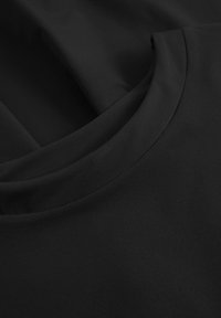 T-shirt noir présentant une texture lisse et douce avec un col rond et un détail de coutures subtiles le long du col et des épaules.