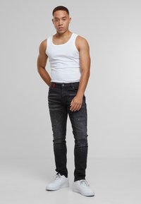 Crne iznosene traperice s plavim mrljama boje, uski kroj, pet džepova, uparene s bijelim topom bez rukava i bijelim tenisicama.