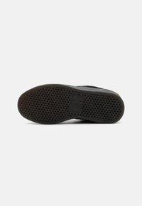 Semelle en caoutchouc noir avec une surface texturée présentant un motif géométrique et un logo de marque embossé. Conception durable et flexible.