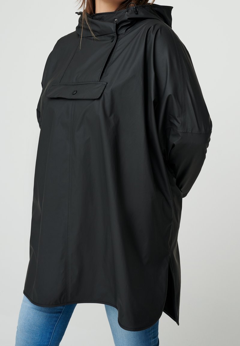 Sort vandtæt oversized jakke med forlommer, justerbar hætte og sideslidser; glat tekstur og afslappet pasform.