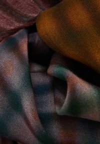 Tela multicolorida con una textura suave y lisa; presenta tonos de marrón, verde y morado; dispuesta en pliegues.