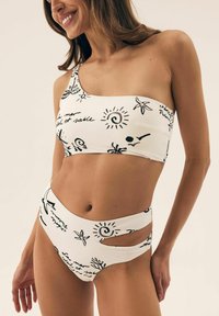 Biały kosztium kąpielowy z czarnymi nadrukowanymi wzorami, z górą na jedno ramię oraz wysokim stanem z wycięciami po bokach.