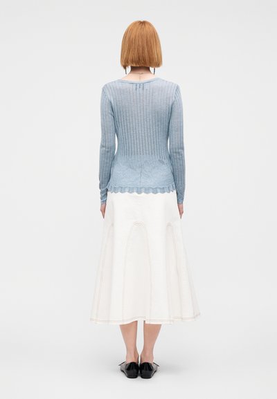 Pull en maille côtelée bleu clair avec ourlet festonné, associé à une jupe blanche évasée avec coutures visibles. Des chaussures plates noires complètent le look.