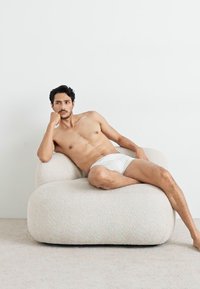 Scaun ondulat, texturat, de culoare crem cu o suprafață pufoasă, având o persoană relaxându-se, îmbrăcată în lenjerie albă, pe un fundal deschis.