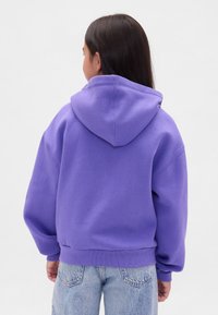 Sweatshirt roxo com capuz grande ajustável, ombros caídos e punhos canelados. Combinado com jeans azul claro de cintura alta.