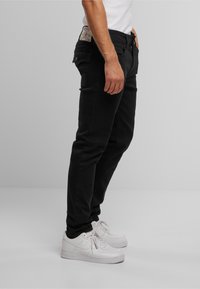 Jeans negri cu croi slim, din denim, având fermoar la zip, cinci buzunare și o etichetă pe talie în spate. Purtați cu adidași albi.