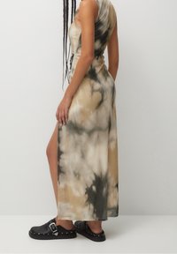Vestido maxi de tie-dye en tonos beige y gris, con una abertura lateral y un diseño ajustado. Calzado negro con detalle de hebilla metálica.