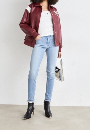Vínově červená bunda z umělé kůže, bílé designové akcenty, bílý přiléhavý top, světle modré úzké džíny, černé špičaté kotníkové boty s kovovým detailem na špičce.