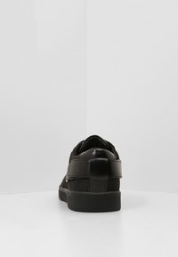 Baskets noires avec une tige en cuir lisse et textile, dotées d'un talon renforcé, d'une semelle en caoutchouc et d'une bride sur le médio-pied.