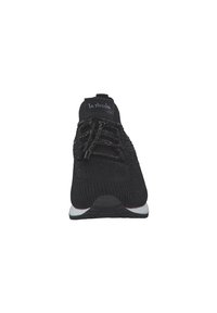 Zapatilla atlética negra de punto con parte superior texturizada, cordones elásticos y suela blanca. Presenta un logo en la lengüeta y un diseño de punta redondeada.