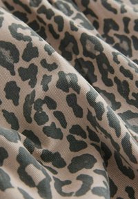 Leopardikuvioinen kangas, jossa on tumman vihreitä laikkuja vaaleanbeige taustan päällä, teksturoitu pinta ja taitettu ulkonäkö.