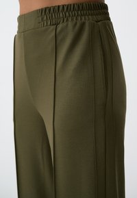 Olijfgroene stretchbroek met een brede tailleband, voorzien van verticale naden voor een gepolijste uitstraling en een gladde textuur.
