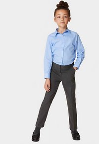 Camicia azzurro chiaro con bottoni, maniche lunghe, abbinata a pantaloni grigio scuro. Tessuto liscio, vestibilità sartoriale, con scarpe nere lucide.