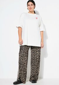 T-shirt bianca a maniche corte con grafica a forma di cuore rosso, abbinata a pantaloni larghi con stampa leopardo. Scarpe flat nere.