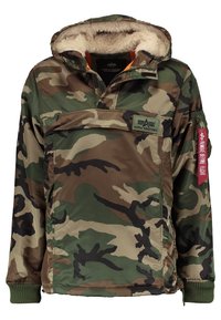Veste à capuche camouflage avec doublure en polaire, grande poche avant, poignets côtelés et étiquette rouge "Remove Before Flight" sur la manche gauche.