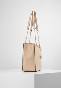 Béžová syntetická taška přes rameno s dvojitými ramenními popruhy a zlatými řetízkovými akcenty. Má hladký povrch a černé lemování podél švů.