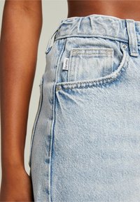 Light blue denim skirt with a high waist, frayed hem, and a subtle texture. Features front pockets and a tag with the brand name.