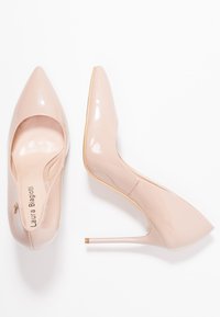 Nude patentläder högklackade skor med spetsiga tår, en gulddetalj på klacken och en slät, glänsande yta. Elegant designad med en strömlinjeformad silhuett.