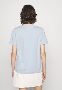 Camiseta de algodón de color azul claro con mangas cortas, cuello redondo y un corte relajado, combinada con una falda de mezclilla blanca, vista desde la parte posterior.