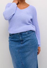 Pull en tricot violet clair avec col en V et manches longues, associé à une jupe en denim avec des détails de coutures diagonales.
