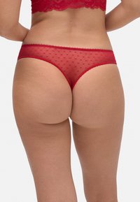 Tanga de encaje rojo semitransparente con un patrón de puntos, con bordes festoneados y un diseño de corte bajo adecuado para el uso diario.