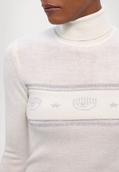 Gai bēšs turtlenecks džemperis ar teksturētu adījumu, ar horizontālām pelēkām svītrām un dekoratīviem motīviem ar rokām un zvaigznēm.