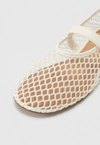 White mesh sandal featuring a honeycomb pattern, with a wide strap across the foot and a smooth brown insole for comfort.