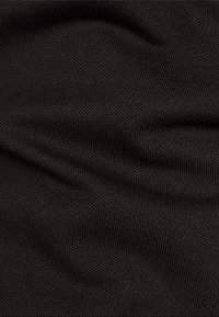 Musta teksturoitu kangas, jossa on hieno ribbiohje, pehmeä pinta ja kevyt kiilto, aseteltu esittelemään sen joustavuutta ja liikettä.