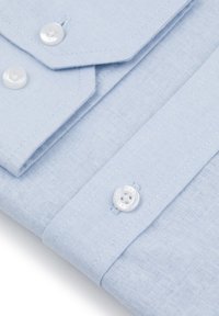 Jasnoniebieska koszula z teksturowanej tkaniny, z wyraźnym kołnierzykiem, dwoma guzikami i kontrastującymi szwami wzdłuż listwy.