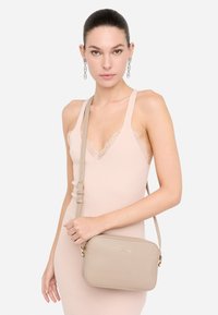 Borsa a tracolla beige con una texture liscia, forma rettangolare e dettagli in metallo dorato. Cintura regolabile e discreto logo.