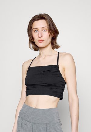 Top cropped preto com alças finas, apresentando um tecido texturizado com detalhe franzido. Combinado com uma parte inferior de cintura alta em cinza claro.