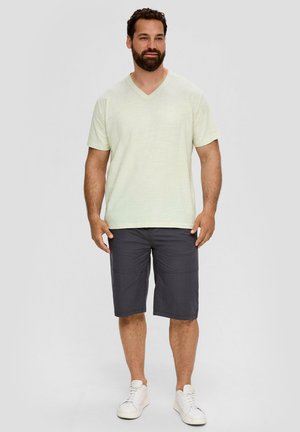 Hellgrünes V-Ausschnitt-T-Shirt, kombiniert mit dunkelgrauen Shorts und weißen Sneakers. Der Stoff wirkt angenehm und hat einen lockeren Schnitt.