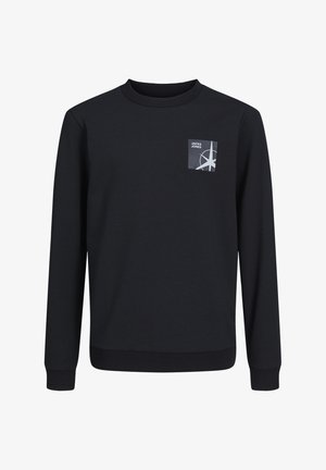 Marineblå sweatshirt med lille grafik ved brystlommen, kombineret med khakibukser og sorte sneakers med hvide tåkapper. Enkelt design og pasform.